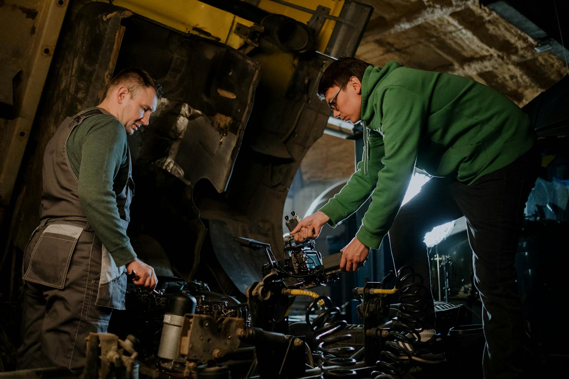 Two mechanics engaged in repairing an engine, showcasing teamwork in an industrial setting.