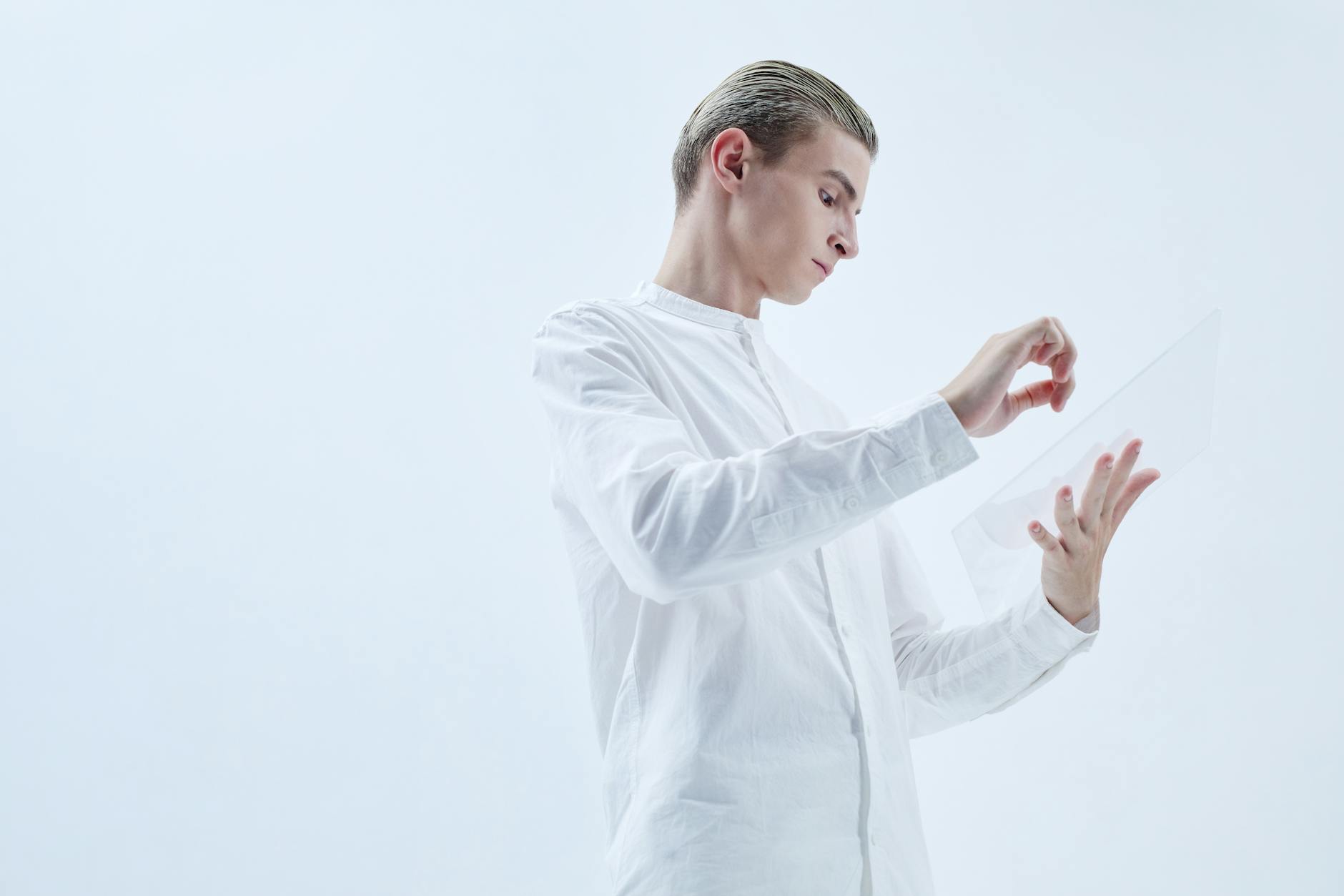 Young man interacting with a transparent digital tablet in a minimalist studio setting.